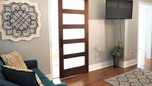 A living room with a sliding barn door, a mounted TV, a patterned rug, and a decorative wall piece. - Location! Location! Location!  (Houston)