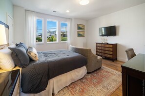 Un dormitorio con una cama grande, un aparador, un televisor y una ventana con vistas a casas.