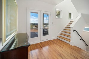 A modern interior with a wooden staircase, glass doors leading to a balcony, and a glass-top desk.