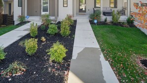 Een woonhuis met twee verdiepingen, een voortuin met beplanting, een overdekte entree en een geplaveid pad.