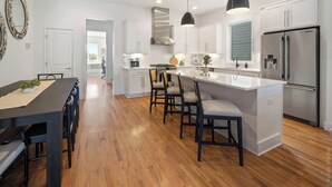 Een moderne keuken met witte kasten, een centraal eiland met barstoelen, een roestvrijstalen koelkast en hanglampen.