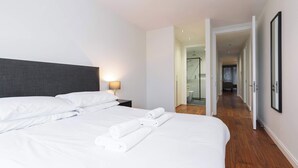 Una habitación de hotel con una cama bien hecha, una mesita de noche con una lámpara y un pasillo que lleva a un baño.