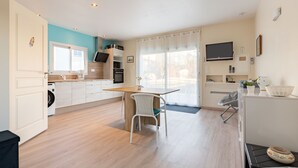 A modern kitchen with a dining area, a washing machine, and a TV mounted on the wall.