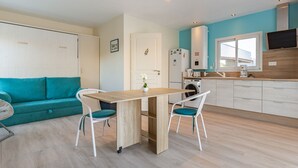A modern kitchen with a dining area, a teal sofa, and a TV mounted on the wall.