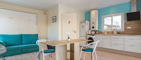 Une cuisine moderne avec un coin repas, un canapé de couleur turquoise et un téléviseur fixé au mur.