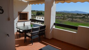 Varanda com mesa e cadeiras, forno de tijolo e vista para uma paisagem verde com montanhas.