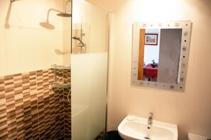 Une salle de bain avec une douche, un lavabo entouré de parois en verre et un miroir doté d’un cadre décoratif.
