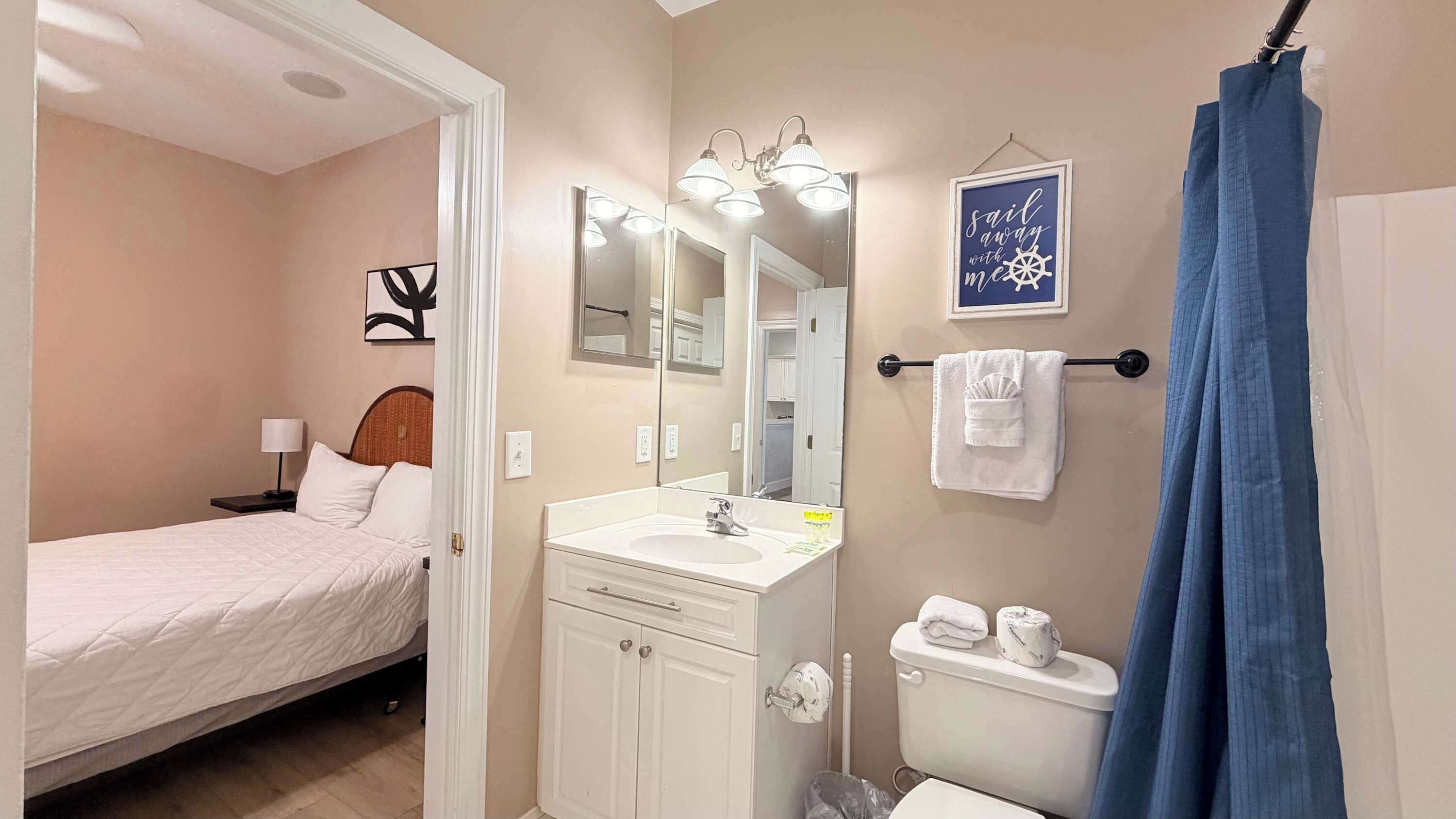 A hotel room with a bed, a bathroom with a sink, mirror, and a towel rack.