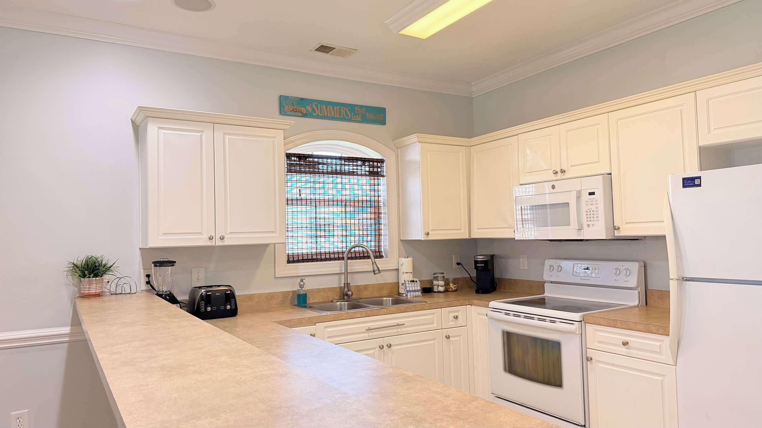 A kitchen with white cabinets, a microwave, a stove, a sink, and a window with a grid pattern.