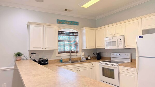 A kitchen with white cabinets, a microwave, a stove, a sink, and a window with a grid pattern.