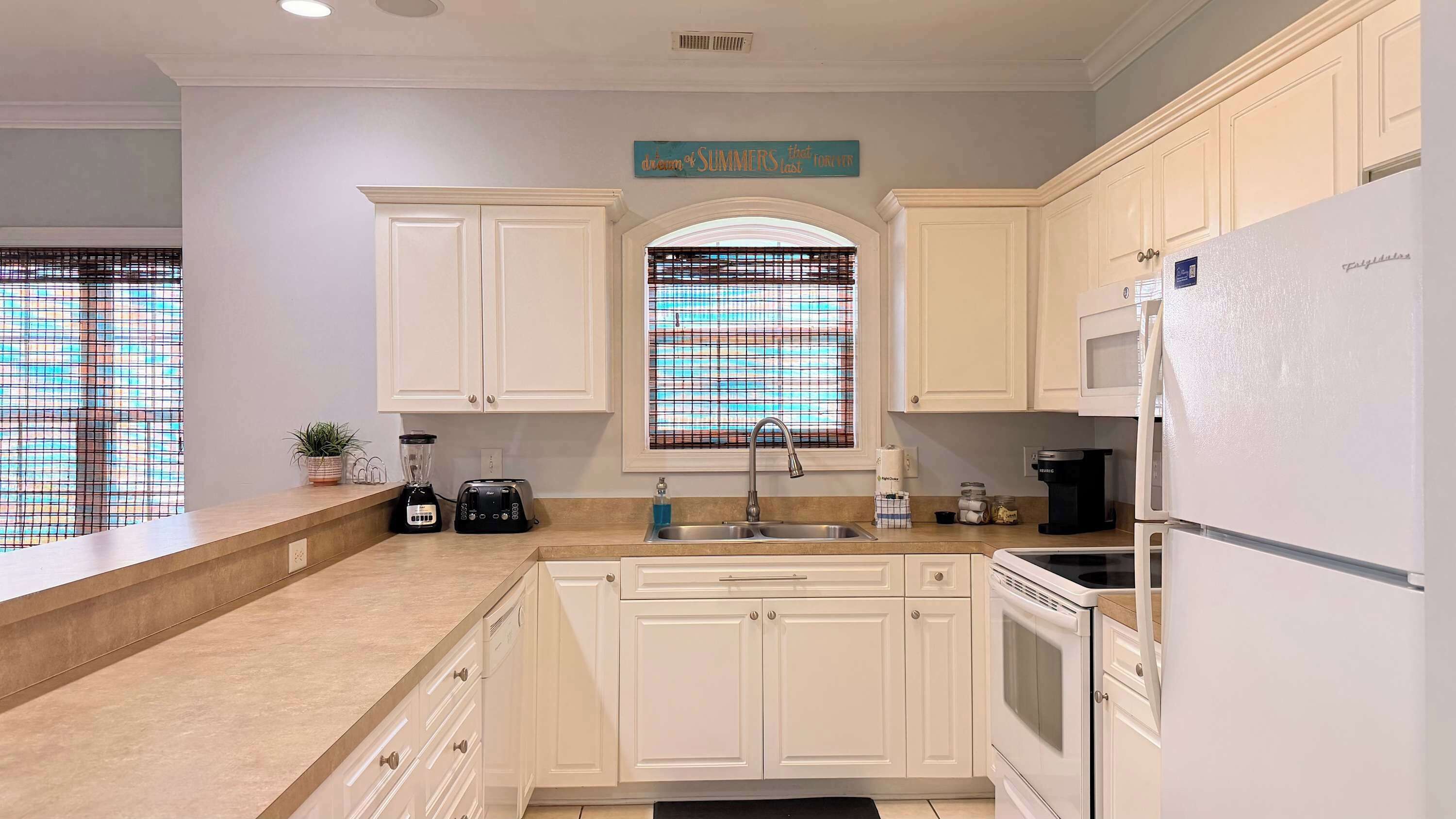 A kitchen with white cabinets, a built-in oven, a refrigerator, a toaster, and a window with a view.