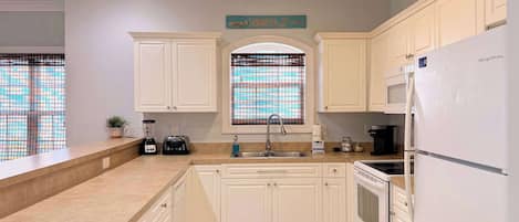 A kitchen with white cabinets, a built-in oven, a refrigerator, a toaster, and a window with a view.