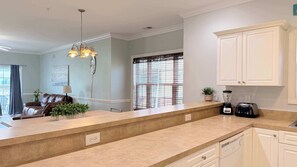 A kitchen with a countertop, a dining area with a sofa, and a window with a curtain.