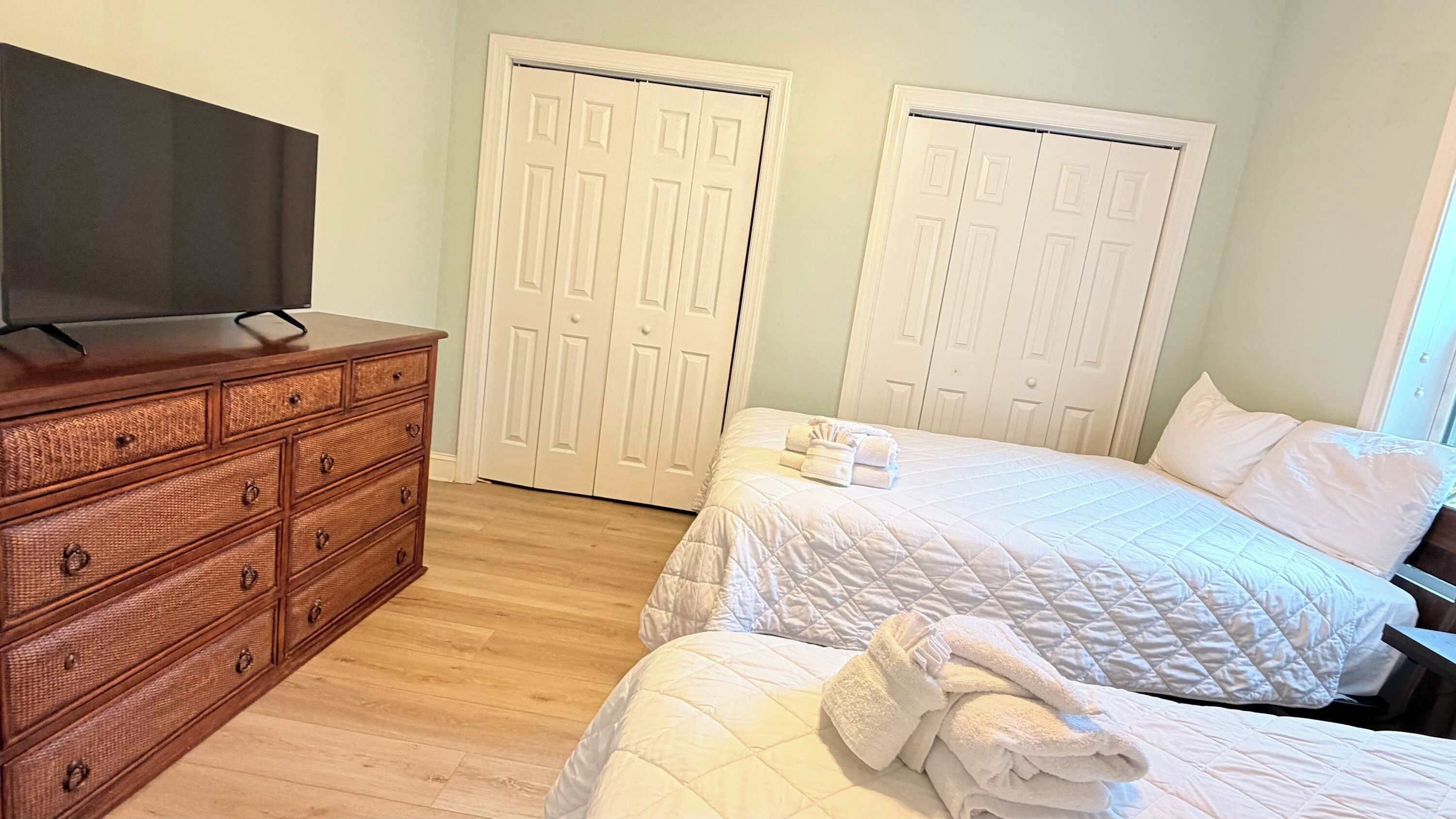 A bedroom with a wooden dresser, two beds with white bedding, and white double doors.