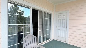 Une véranda couverte avec une porte-fenêtre coulissante, une porte blanche et une chaise.
