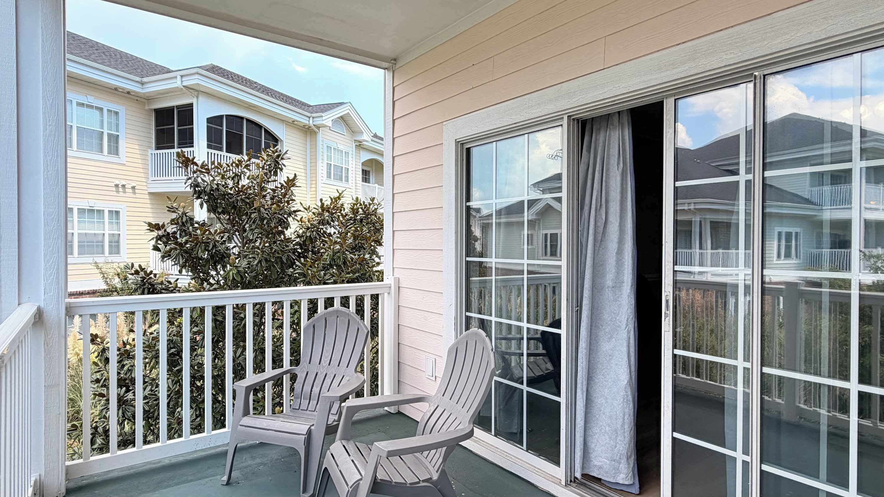 A balcony with two Adirondack chairs, a view of neighboring houses, and a large sliding glass door.