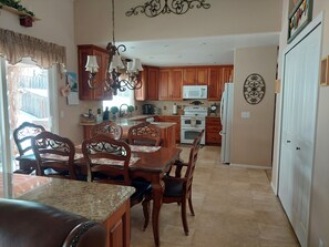 A kitchen with wooden cabinets, a granite countertop, a chandelier, and a dining area with a table and chairs.