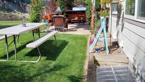 Un jardin avec une pergola en bois, un espace barbecue et une terrasse avec une table et des chaises.