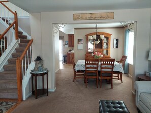 A dining area with a wooden table, chairs, and a chandelier. A staircase with wooden railings is visible on the left.