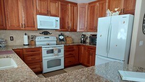 Une cuisine avec des meubles de rangement en bois, une cuisinière blanche, un four à micro-ondes, un réfrigérateur et des plans de travail en granit.