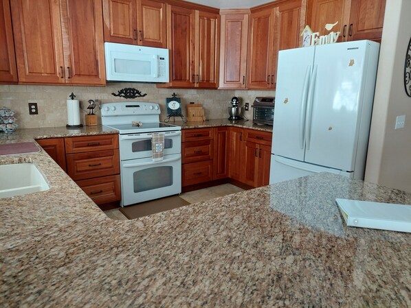 Una cocina con armarios de madera, estufa blanca, microondas, refrigerador y encimeras de granito.