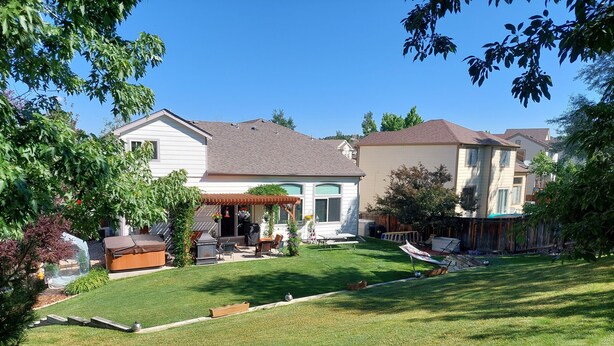 Un jardin à l’arrière d’une maison, aménagé avec une terrasse, un barbecue et du mobilier d’extérieur.