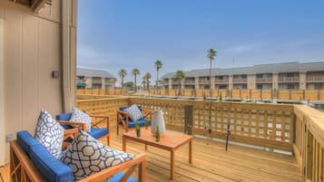 A wooden deck with blue cushioned seating and a table, overlooking a row of buildings with palm trees.