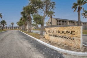 Une enseigne pour le Bay House, située sur Broadway, avec une route dégagée et des palmiers en arrière-plan.