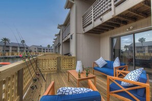 A wooden deck with outdoor furniture, fishing rods, and a view of buildings in the background. - A Fishers ParadiseW/Boatdock! (Rockport)
