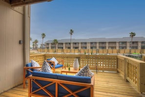 Une terrasse en bois avec des sièges rembourrés bleus, un vase et une vue sur un bâtiment d’hôtel bordé de palmiers.