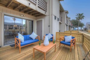 Une terrasse extérieure avec des canapés bleus et des chaises en bois, une table en bois et une porte vitrée donnant sur un espace patio.
