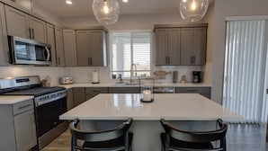 A modern kitchen with a central island, stainless steel appliances, and pendant lighting. - Happiness Beach Cabin - Oyhut Bay Seaside Village (Ocean Shores)