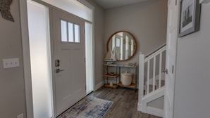 A hallway with a white door, a round mirror, a small console table with decorative items, and a blue and white rug. - Happiness Beach Cabin - Oyhut Bay Seaside Village (Ocean Shores)