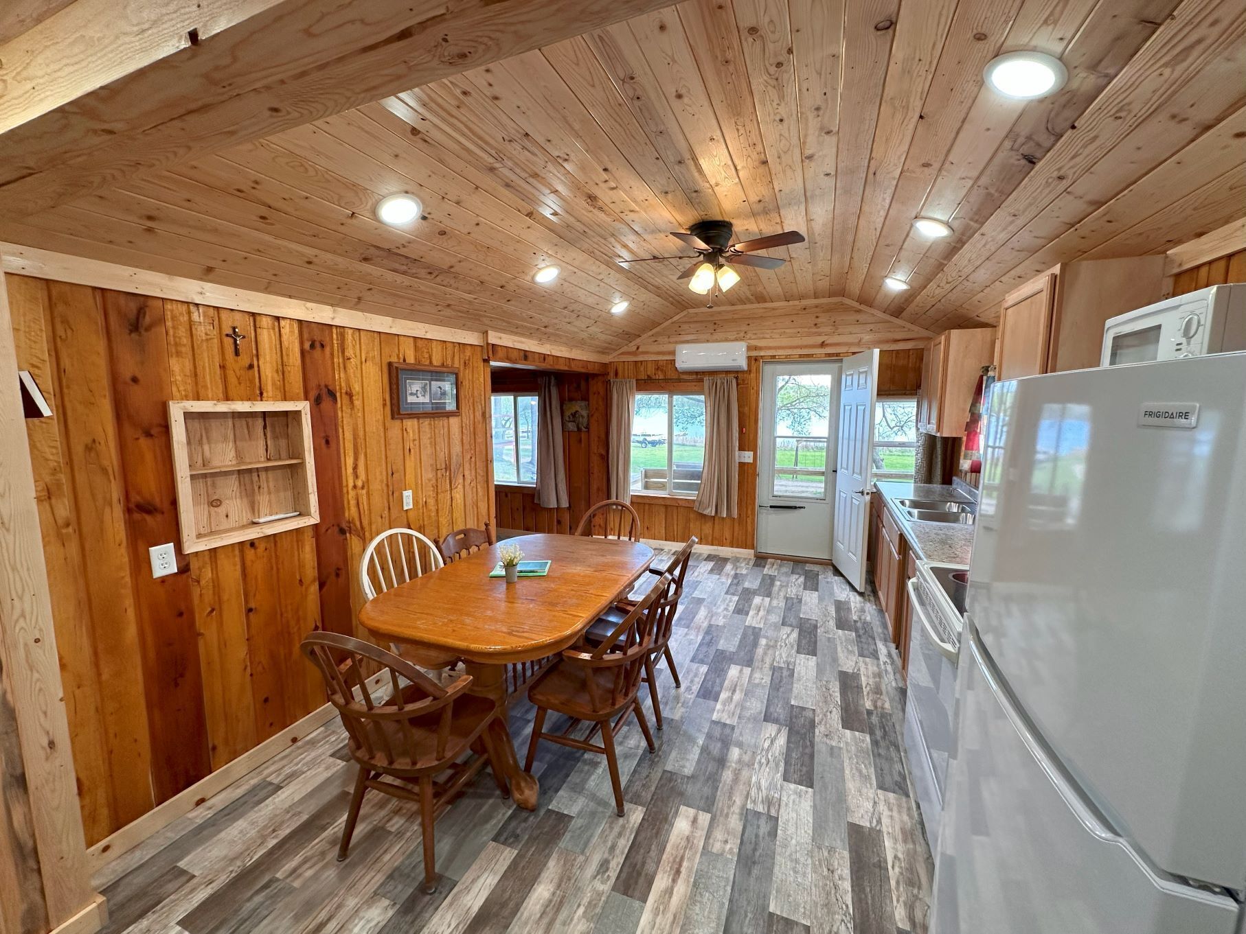 A wooden interior with a dining table, chairs, a ceiling fan, recessed lighting, and a kitchen area with a refrigerator.
