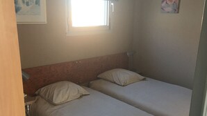 A small, simple room with two single beds, a window, and a lamp. - T2 APARTMENT IN THE CENTER OF TOWN, 5 MINUTES FROM THE SPA (Balaruc-les-Bains)