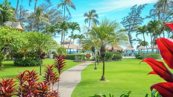A tropical resort with a well-maintained lawn, palm trees, and a pathway leading to a beach area.