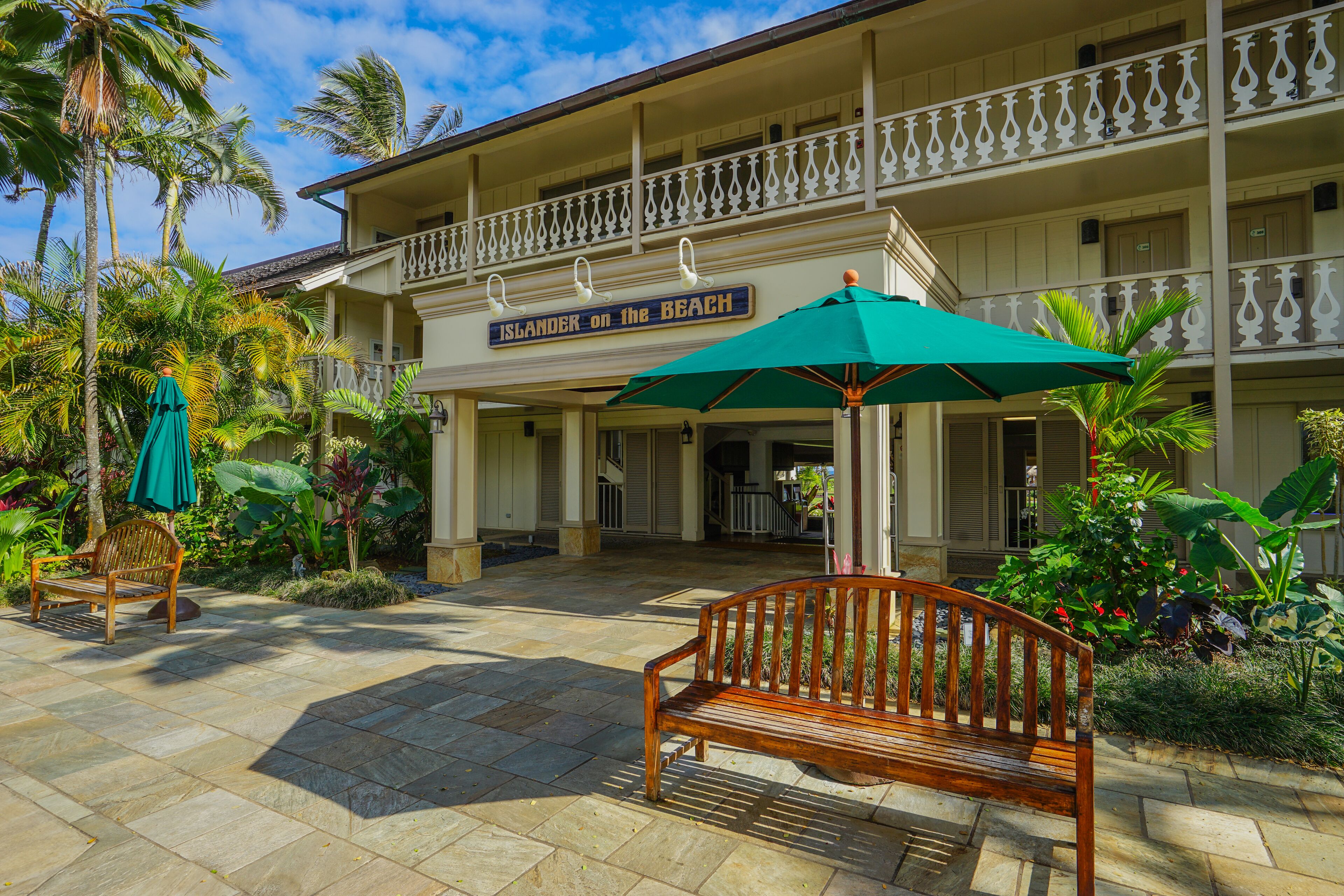 A hotel with a balcony, a wooden bench, and a sign that reads "Islander on the Beach".