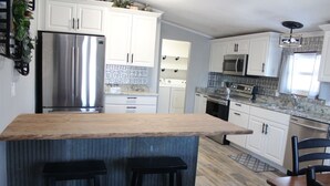 A modern kitchen with white cabinets, stainless steel appliances, and a wooden island with bar stools. - Lake View cottage, secluded, quiet, total remodel, 3 king beds (Wagoner)