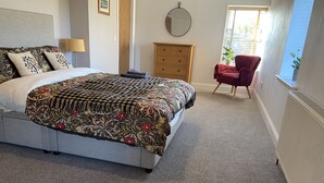 Een slaapkamer met een groot bed, een houten dressoir, een rode stoel en een raam met uitzicht.