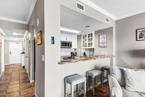 A modern kitchen with white cabinets, a microwave, and a coffee maker. There are two bar stools and a countertop with a patterned backsplash.