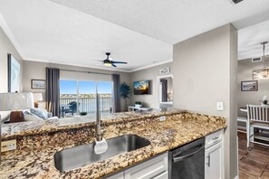 A modern kitchen with a granite countertop, stainless steel sink, and a ceiling fan. - ✈️ 🌊 South Harbour 6C: Blue Angels, Water Views + Walk to the Boardwalk! (Pensacola Beach)
