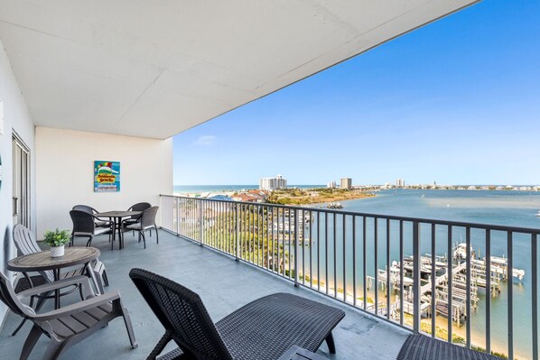 A balcony with outdoor furniture, a view of the sea, and a building in the background.