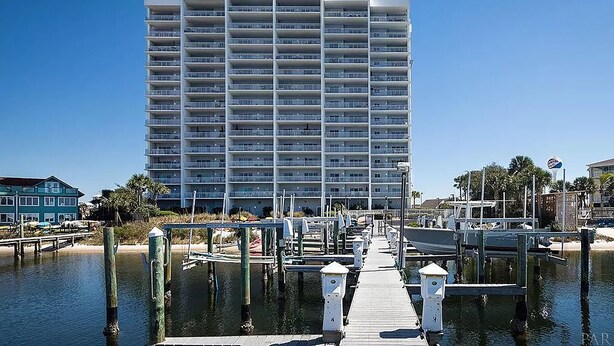 A multi-story hotel with a dock extending into calm water, surrounded by palm trees and other buildings.