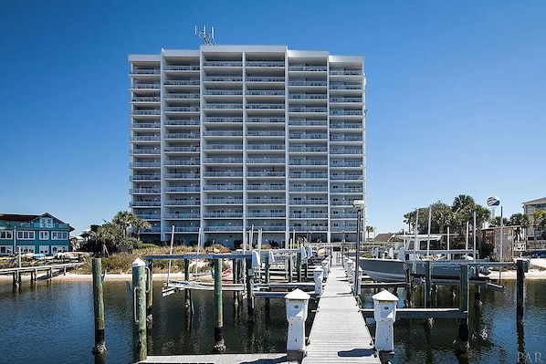 Un hotel de varios pisos con un muelle que se adentra en aguas tranquilas, rodeado de palmeras y otros edificios.