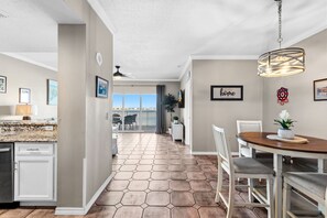 A modern kitchen with a granite countertop, a dining area with a wooden table, and a view of the ocean through large sliding doors. - ✈️ 🌊 South Harbour 6C: Blue Angels, Water Views + Walk to the Boardwalk! (Pensacola Beach)