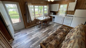 Een gezellig cabin interieur met een eethoek, keuken en een groot raam met uitzicht op een grasveld.