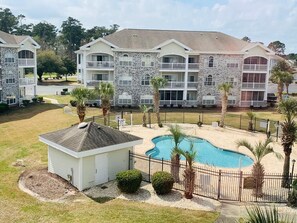 A multi-story hotel with a swimming pool surrounded by palm trees and a fenced area. - Pond view beautiful apartment at Magnolia Place (Myrtle Beach)