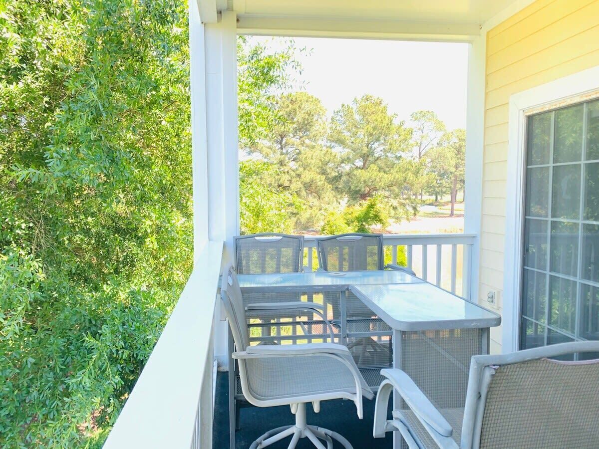 Une terrasse couverte, dotée d’une table et de chaises, et entourée de verdure.