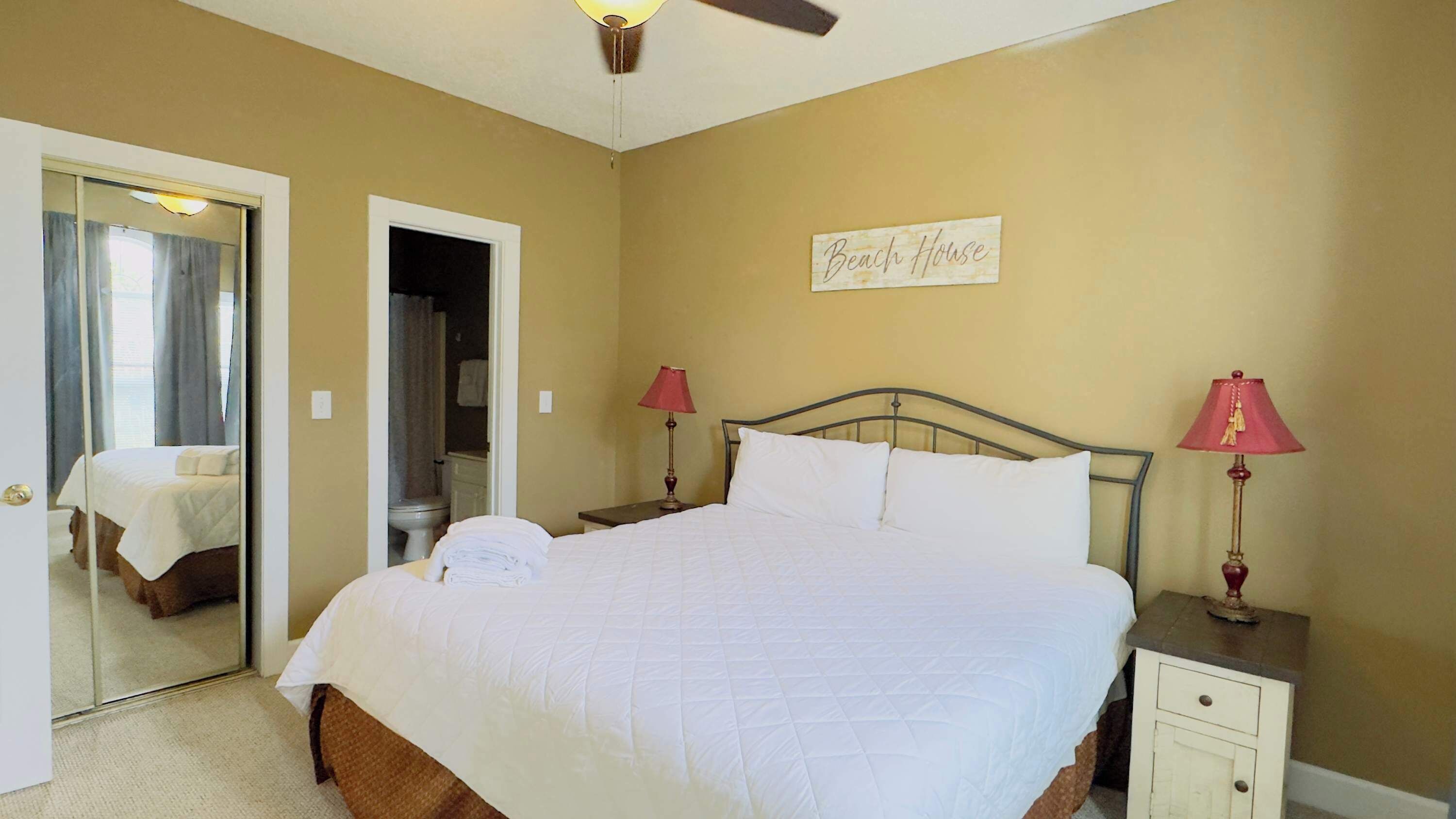 A neatly arranged bedroom with a bed, two bedside tables, a nightstand, a ceiling fan, and a mirror.
