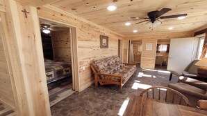 L’intérieur d’un chalet en bois comprend un lit, un canapé, une table à manger et un ventilateur de plafond.
